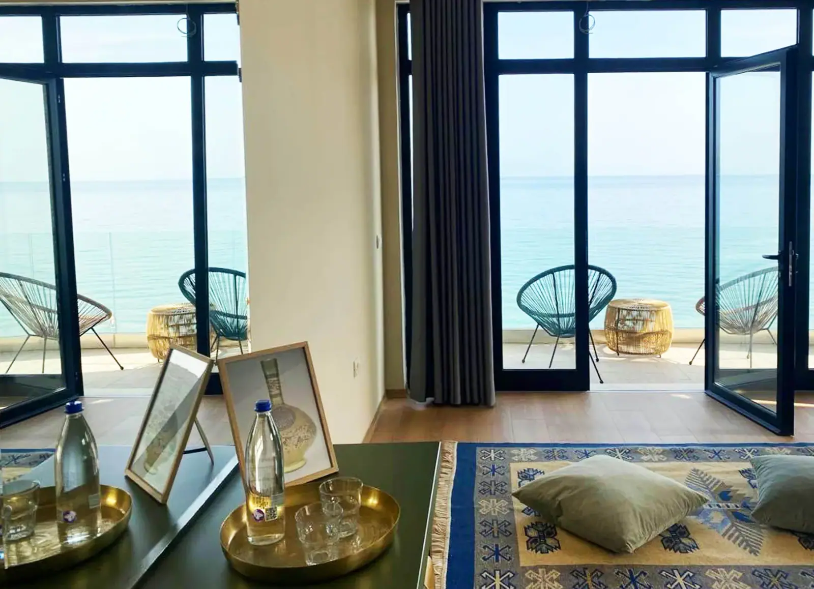Black-framed glazed doors standing open onto a terrace at beach level with the sea beyond