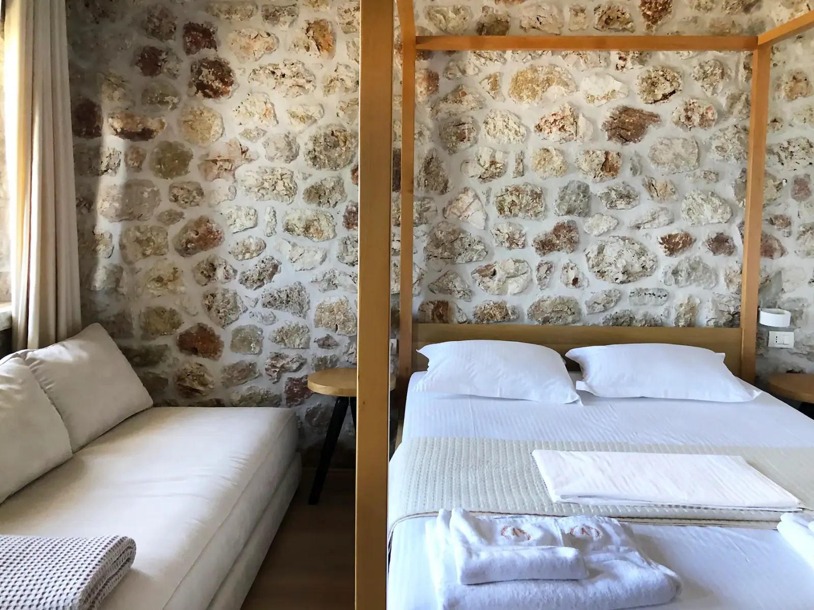 A sofa bed beside a double bed under a timber four-poster frame in a stone-walled room