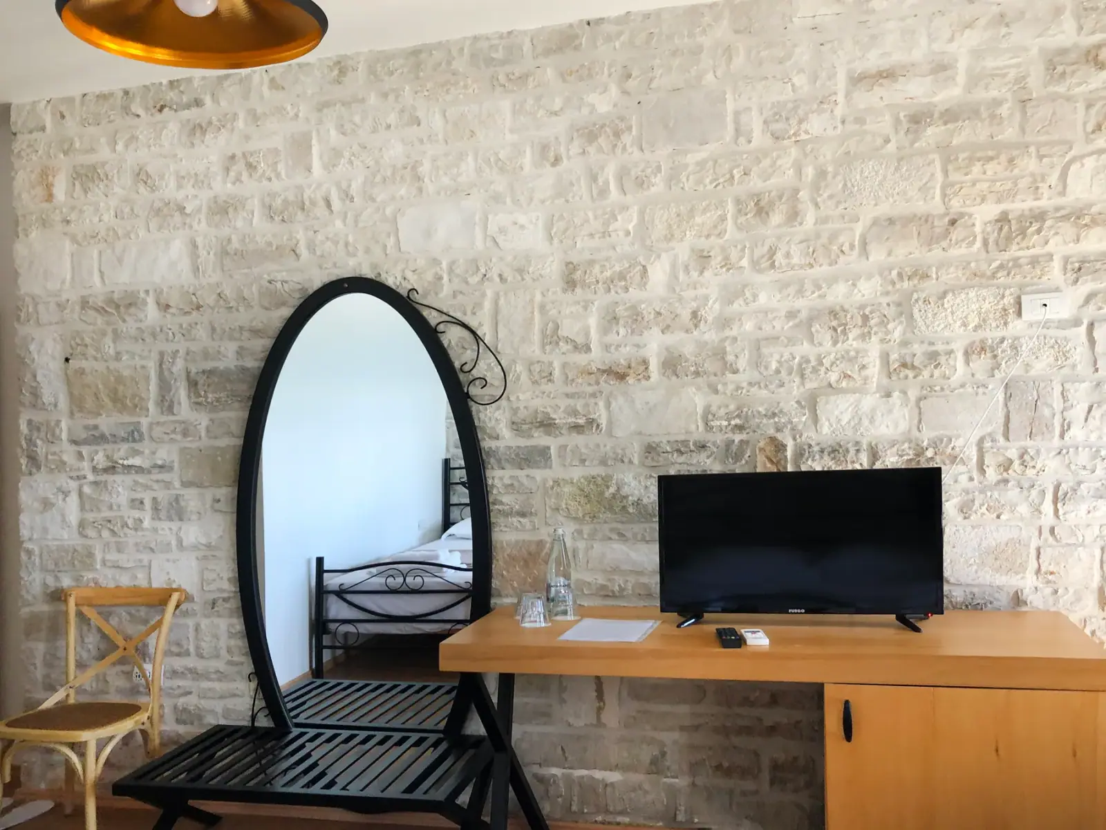 An oval mirror, a writing desk and a television on a limestone wall beside a folding chair