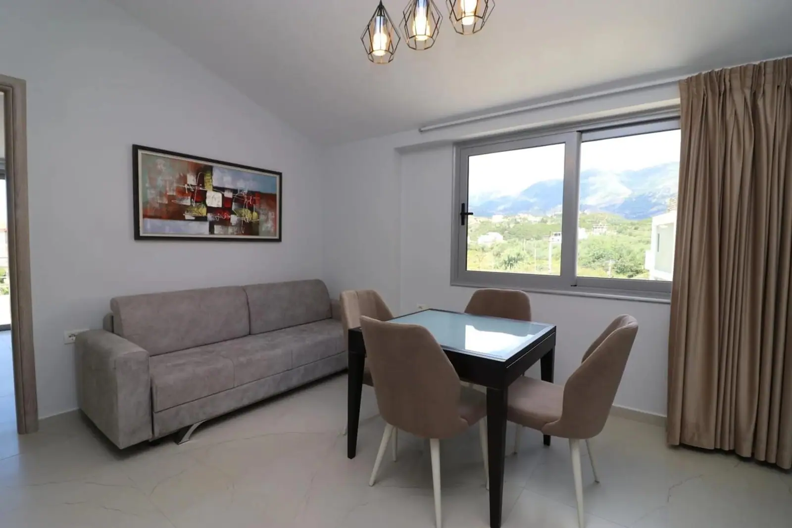 Apartment living room with a sofa, dining table and a window onto the mountains