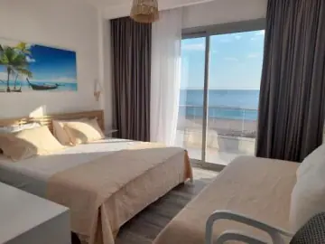 A sea-view room with a double bed and a second bed, its balcony door opening onto Livadhi Beach and the Ionian beyond.