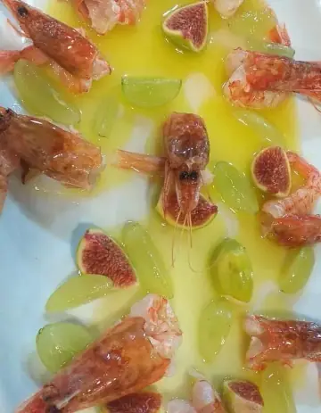 Prawns arranged with quartered figs and green grapes in a pool of olive oil on a white plate