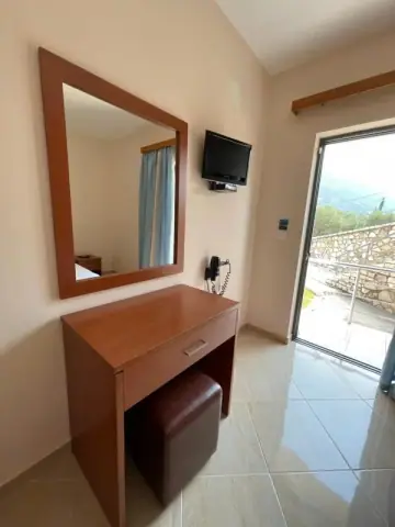 A desk and mirror beside a flat-screen television and a sliding balcony door opening onto a stone wall and the slope beyond