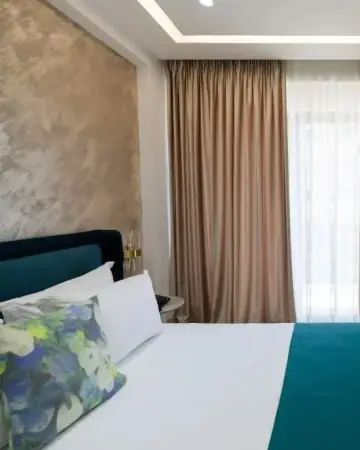 A bed in the deluxe family suite at Chimaera Hotel with a teal throw, a floral cushion and a polished stucco headboard wall