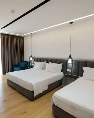A quadruple room at Chimaera Hotel with two beds, a teal armchair and pendant lamps over the bedsides