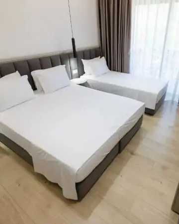 A triple room at Chimaera Hotel with a double bed and a single bed against a padded headboard wall