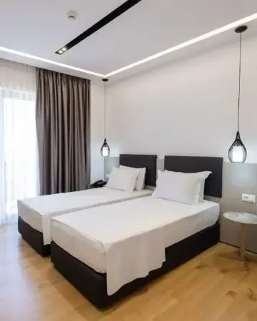 A twin room at Chimaera Hotel with two single beds, glass pendant lamps and a balcony door behind a grey curtain