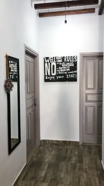 A whitewashed corridor at Himara Downtown Hostel with a tall mirror, painted doors and the hand-painted rules board on the far wall