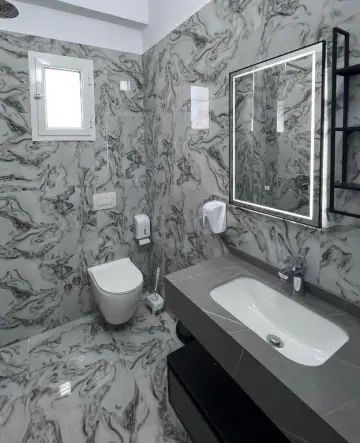 A bathroom at Hotel Frida clad in heavily veined marble, with a lit mirror