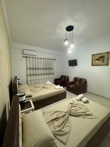 A room at Hotel Frida with two beds either side of a bedside table, two armchairs and a wall-mounted television showing football