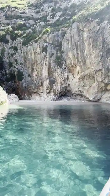 Pebble shore and clear water below the cliff at the Blue Cave