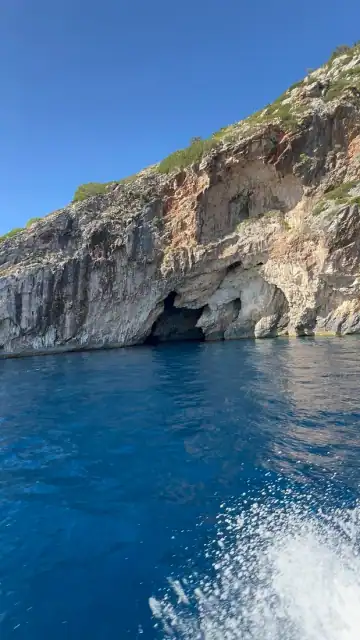 Cave openings in the limestone cliff above deep blue water