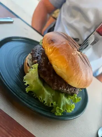 A burger in a glazed bun on a dark green plate over green leaf lettuce, a serrated steak knife pushed through the top