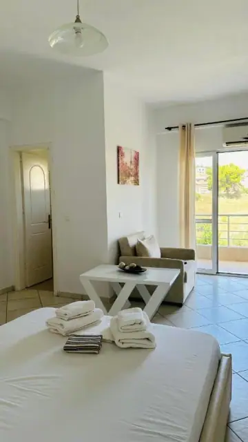 The end of a bed, a sofa and a coffee table beside a sliding balcony door with a green hillside beyond