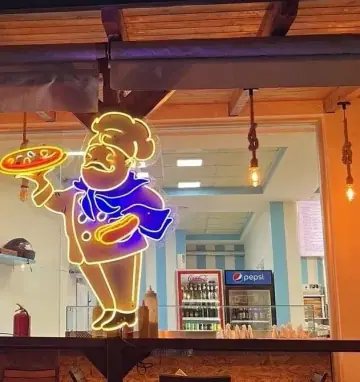 The cook in neon over the counter — a figure outlined in gold, in a buttoned chef's jacket and hat, blue neckerchief, carrying a pizza flat on one hand — with the rope-hung bulbs and the blue and white striped wall behind