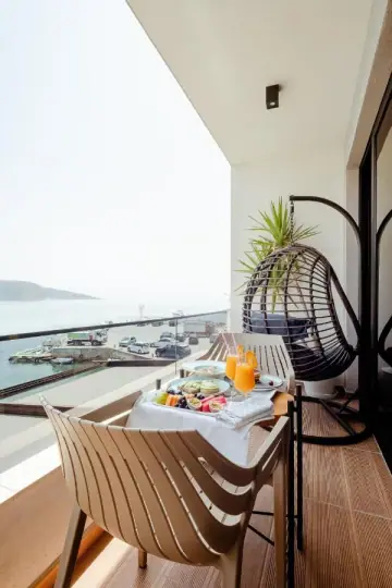 Breakfast laid on a balcony table with a hanging egg chair, above a quay with parked lorries and the sea beyond
