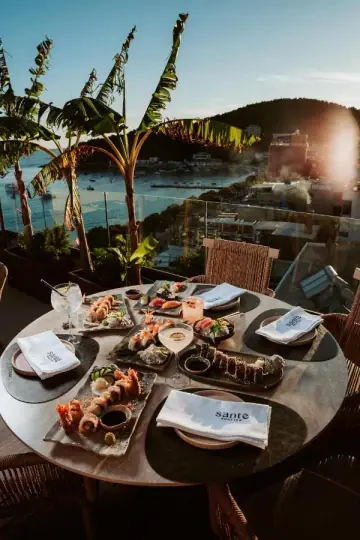 Sushi and sashimi on a round table on the roof, palms and the bay behind