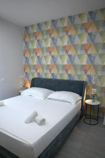A double bed with a slate-blue velvet headboard against a multicoloured triangle feature wall