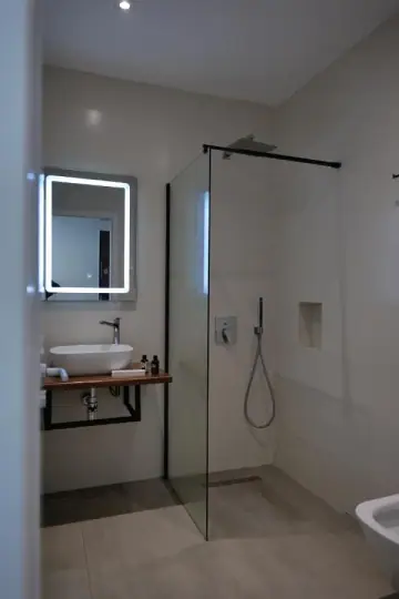 A bathroom with a walk-in rain shower behind glass and a backlit square mirror over a vessel basin