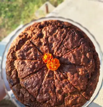 A whole dark cake on a glass stand, cut into wedges and topped with two marigolds