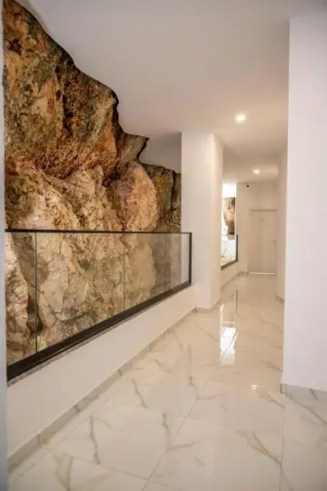A white marble corridor at Wait 'n Sea running alongside the bare excavated rock face, held back behind a glass rail