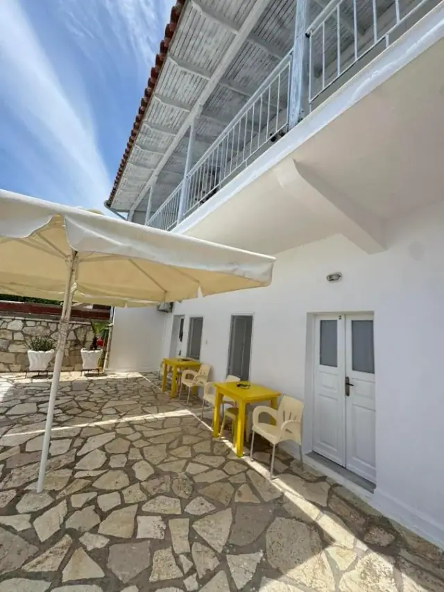 Shaded flagstone courtyard with a parasol, tables and the white doors of the ground-floor apartments