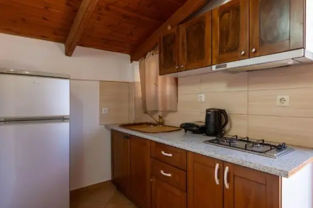 A kitchen with dark timber units, a four-burner gas hob and a tall fridge-freezer under the boarded roof