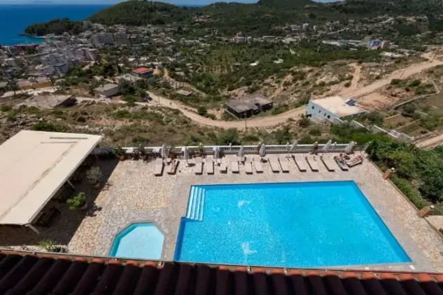Looking down from the hotel roof over the pool deck and its row of loungers to Himarë town, the bay and the headland beyond
