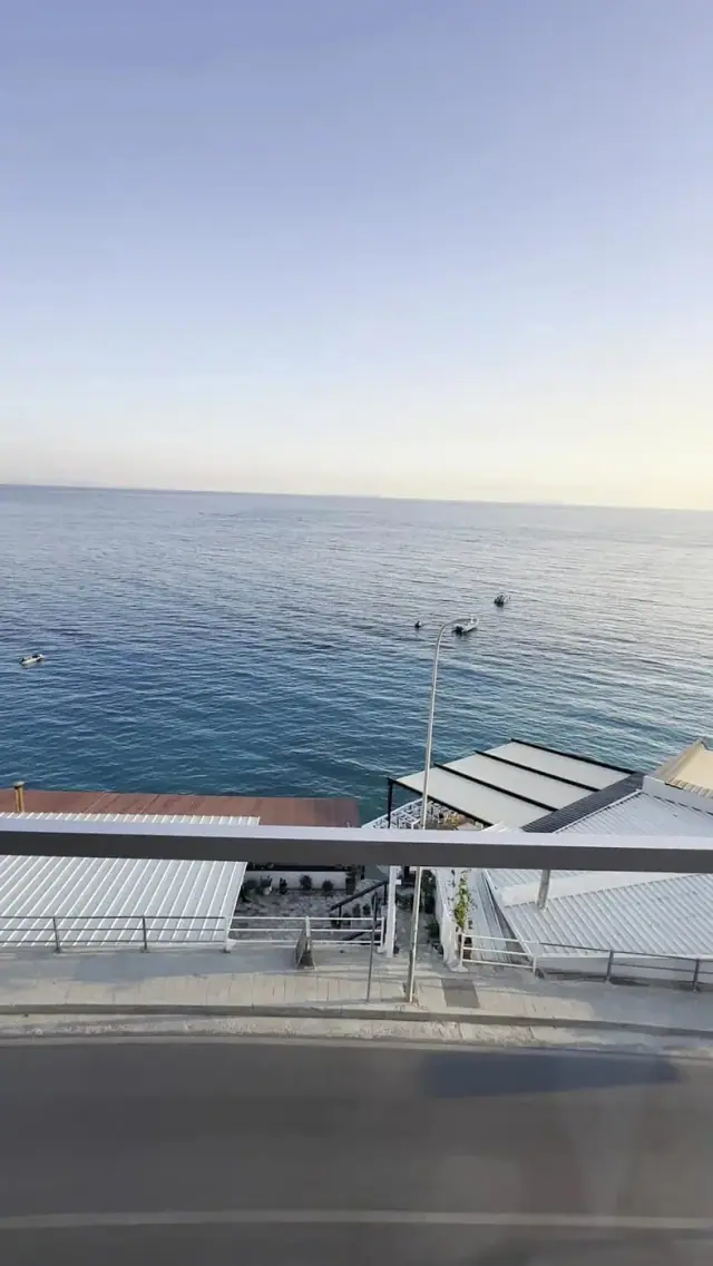 Flat open sea from an upper floor, three boats moored offshore and the beach roofs below