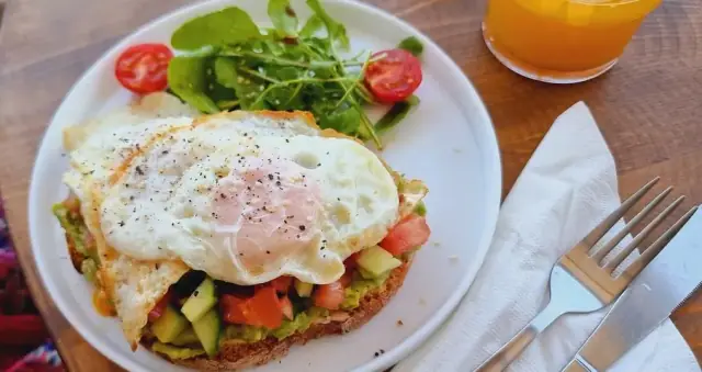 Avocado on toasted sourdough under two fried eggs, with rocket, cherry tomatoes and a glass of orange juice
