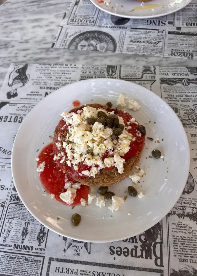 Dakos — a barley rusk topped with grated tomato, crumbled feta and capers — on a newspaper-print placemat at Bar 300