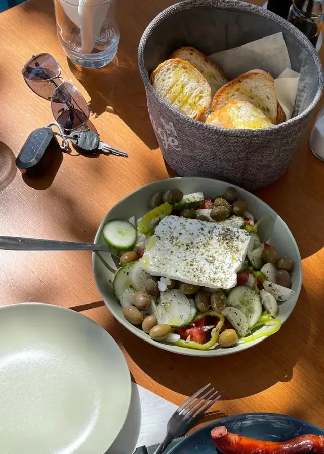 A Greek salad with a slab of feta, a basket of toasted bread and an iced coffee on a table at Bar 300