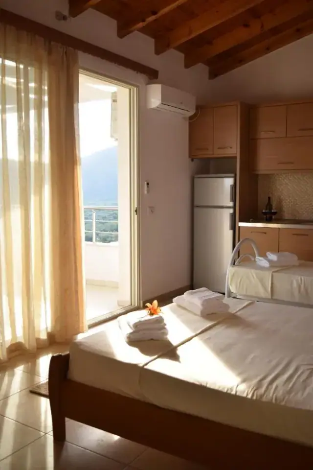 A bed and a kitchenette with a refrigerator, a glazed door open onto a balcony with the mountain beyond
