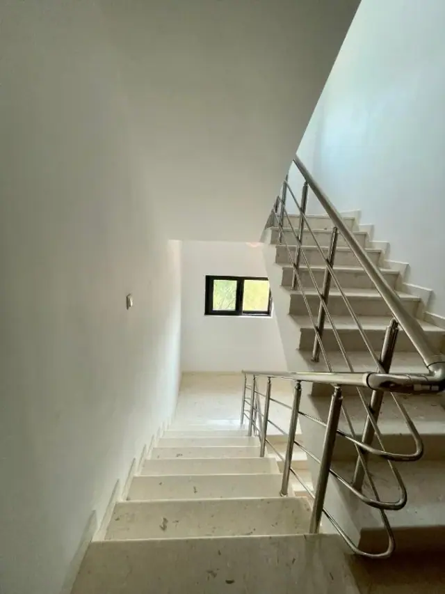A pale travertine staircase with a stainless steel balustrade turning at a landing, lit by a small window on the half-landing wall