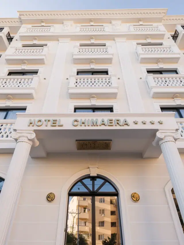 The white entrance front of Chimaera Hotel on Rruga Jorgo Bollano, fluted columns either side of an arched glass door and the hotel's name in relief above it