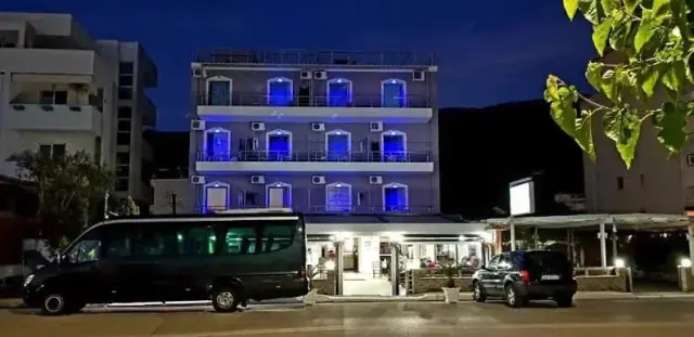 The hotel facade at night, every balcony washed in blue light above the lit restaurant terrace