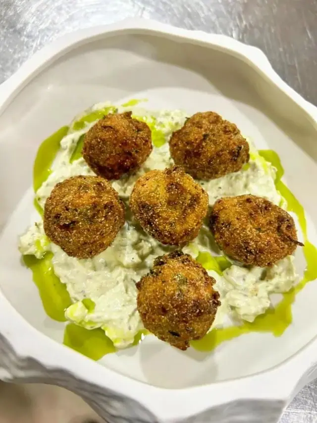 Six fried croquettes on a chunky herbed white dip, dressed with green oil