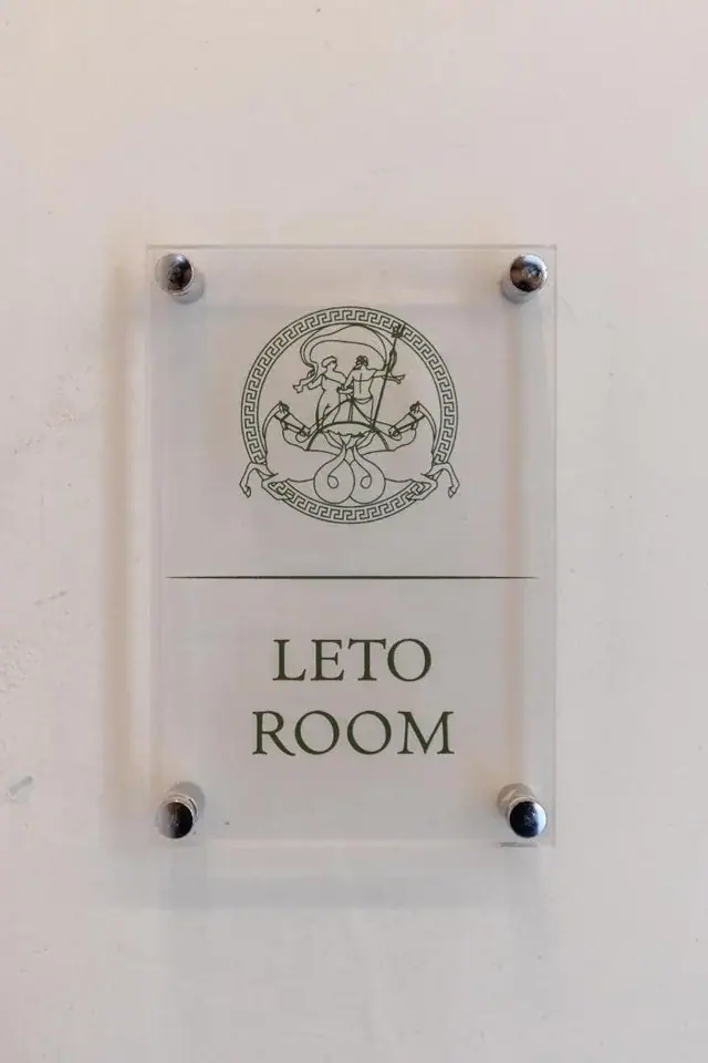 An etched acrylic door plate at Dimitri Hotel, held off the wall on four steel bosses, carrying the green crest above the words LETO ROOM