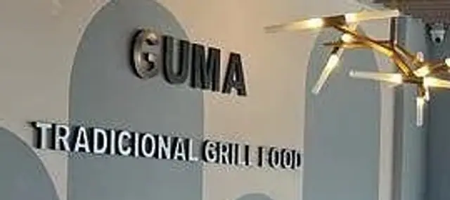 Lettering mounted on the dining-room wall reading GUMA above TRADICIONAL GRILL FOOD, a brass fitting lit at the right