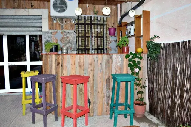 A bar built from salvaged planks at Himara Downtown Hostel with four hand-painted stools in yellow, purple, red and turquoise
