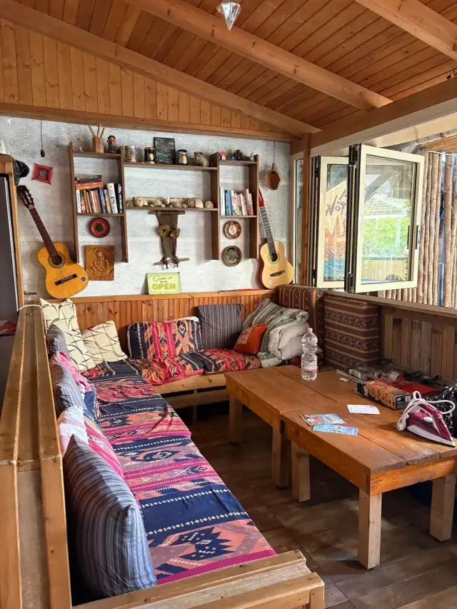 The timber-lined indoor lounge at Himara Downtown Hostel with kilim-covered benches, two guitars on the wall and a shelf of books