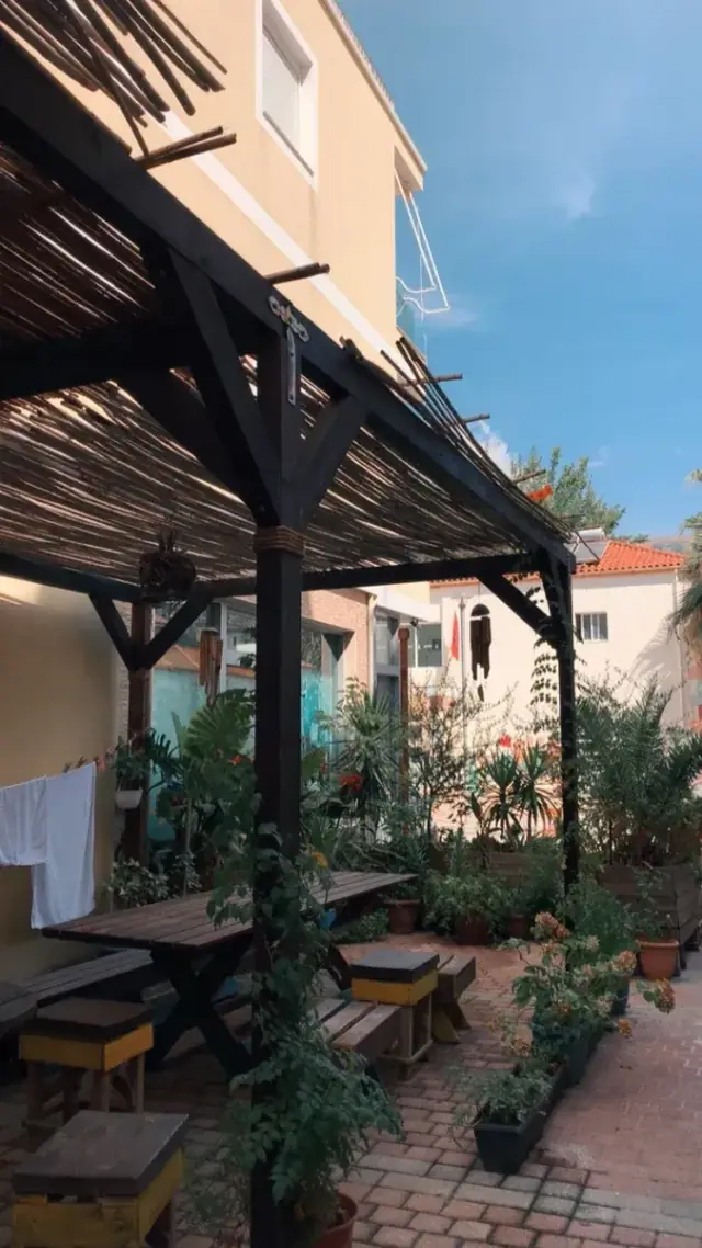 The reed pergola over painted benches and a long table at Himara Downtown Hostel against a clear blue sky