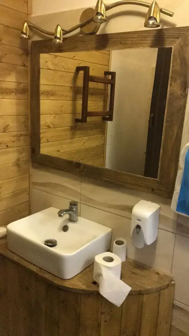 A square basin on a timber counter under a plank-framed mirror and brass lights in a shared bathroom at Himara Downtown Hostel