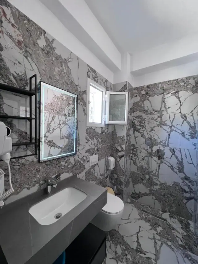 The veined marble bathroom of the Triple Room, with a wall-hung basin and a lit mirror