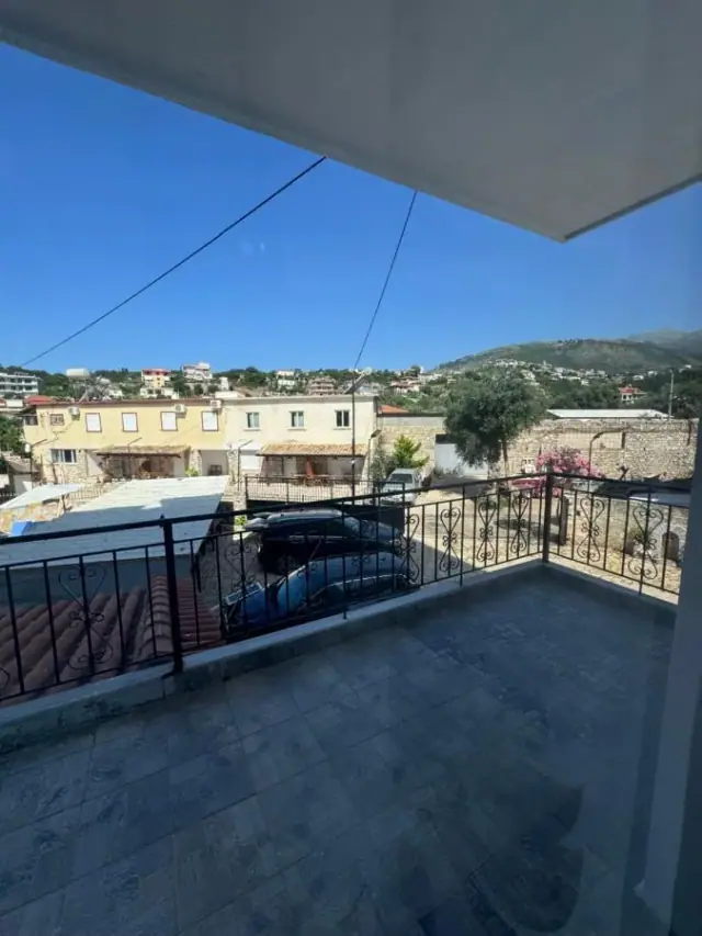 Looking out from a balcony at Hotel Frida past a neighbouring roof to the hillside houses of Himarë and the ridge behind