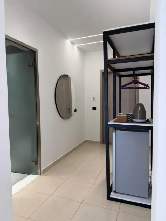An entrance with a round mirror, a hanging rail, a shelf with a kettle and a small refrigerator below