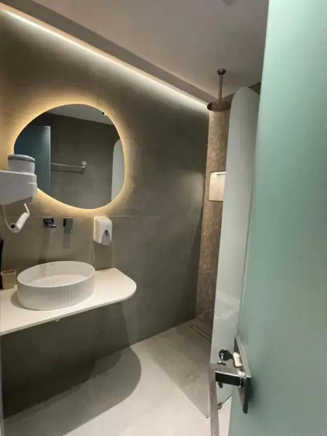 A bathroom in grey micro-cement with an oval basin and a round mirror lit from behind
