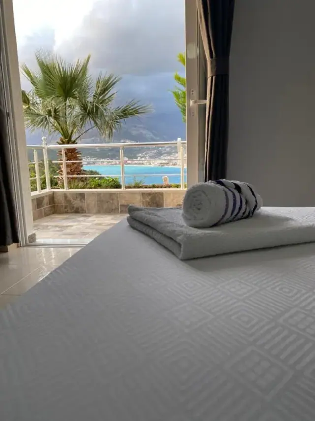 Folded and rolled towels on a made bed, the balcony door open onto a rail with the sea beyond