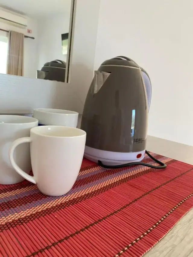 Two white mugs and a kettle on a red woven mat