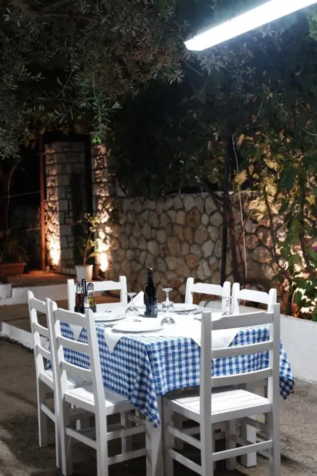 Tables in blue and white checked cloths against a dry-stone wall lit from below, vine overhead